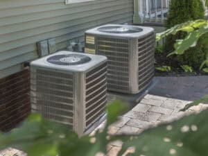 %Imagetitle% | John Nugent &Amp; Sons Two outdoor air conditioning units are placed on a paved area beside a house with siding and brick accents.