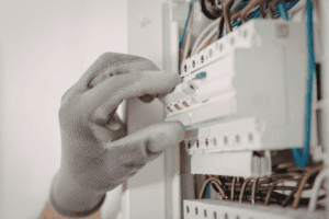%Focuskw% | John Nugent &Amp; Sons A hand wearing a gray work glove flips a circuit breaker switch inside an electrical panel.