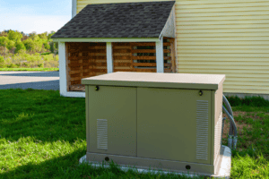 %Focuskw% | John Nugent &Amp; Sons A standby generator sits on a concrete pad next to a yellow house with a covered wood storage area in the background.