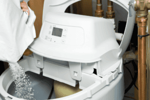 Hand pouring white salt pellets into a water softener brine tank.