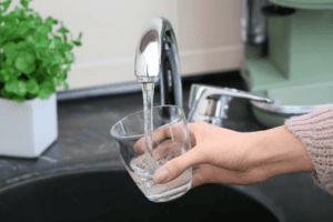 A person fills a glass with water from a kitchen faucet.